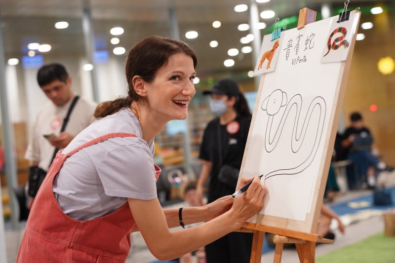 莫尼卡於工作坊示範如何創造出自己的「幻想生物」！她先抽一張「各種品種的狗」的牌卡、再抽一張「其他動物」的牌卡，結果「貴賓蛇」就這樣誕生啦！(高市圖提供)