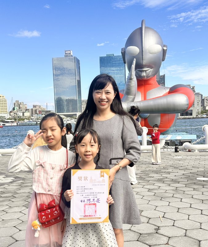 小港高中校長薛鈺勤的小女兒榮獲幼兒園著色比賽的金牌，在媽媽的陪同下光榮上台領獎，母女三人更與超人力壩王開心的合影。(漾新聞記者陳雯萍攝)