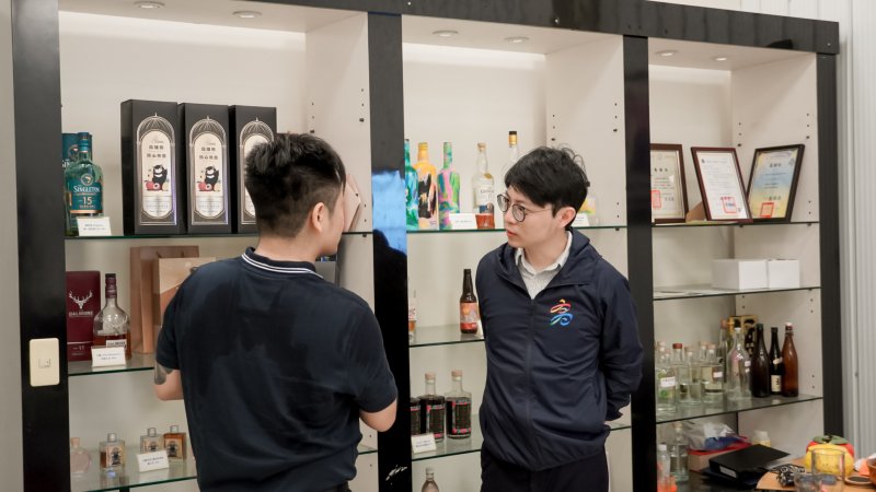 亞耕酒業總經理江岳樓（左）向高雄市政府青年局長林楷軒（右）介紹企業品牌特色，分享如何結合高雄農產（芒果、荔枝、芭樂）研發不同的風味酒。